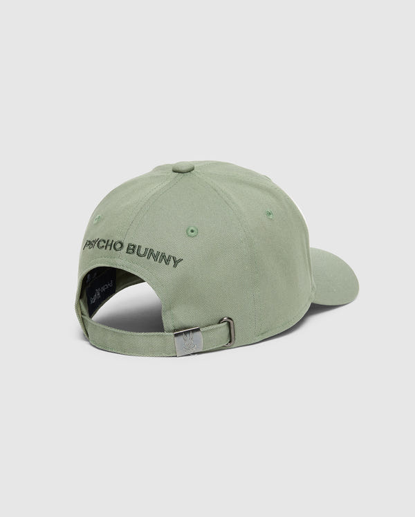 The Psycho Bunny MENS BAXTER EMBROIDERED BASEBALL CAP (B6A552F200) in sage green cotton twill is shown from the back, with "PSYCHO BUNNY" embroidered above an adjustable strap featuring a metal clasp and bunny logo. Light gray background.