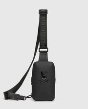 The MENS RUBBERIZED CROSSBODY - B6A635F200 from Psycho Bunny is a durable polyester black bag with "PSYCHO BUN" in raised letters on the strap. It displays a glossy skull and crossbones with bunny ears on the front, set against a plain white background.