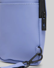 Close-up of the Psycho Bunny MENS RUBBERIZED CROSSBODY (B6A635F200) in light purple polyester, featuring black zipper and hardware, a rabbit head cutout zipper pull, adjustable strap clip at the bottom, and white edge stitching.