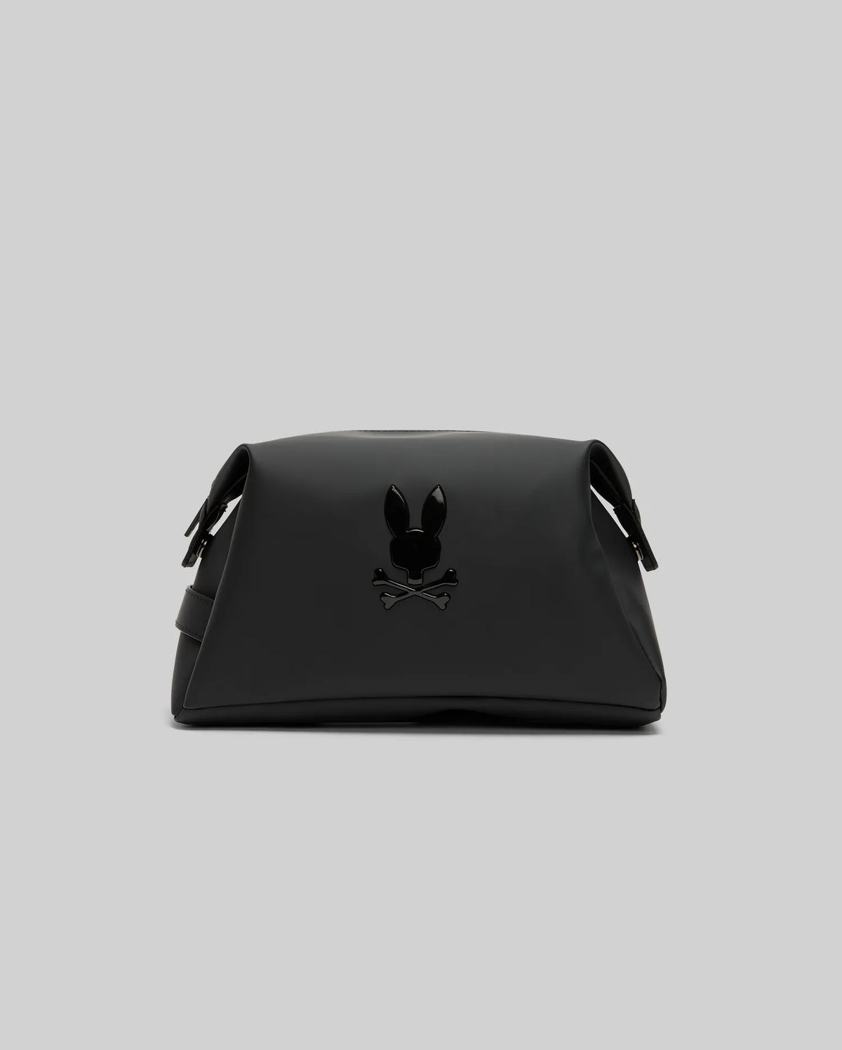 The Psycho Bunny MENS RUBBERIZED TOILETRY KIT (B6A636F200) is a black organizer bag with a glossy black bunny head and crossbones logo on the front, zip closure, and shown against a plain light gray background—perfect for travel essentials.