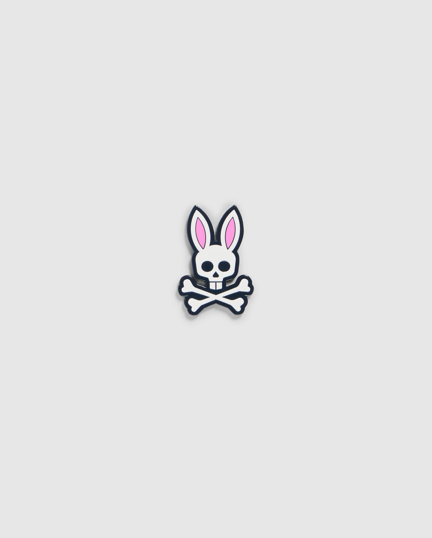 A graphic of a bunny skull and crossbones from the Psycho Bunny golfers collection. The skull has rabbit ears with pink interiors and a small bow tie under the chin. Crossbones form an "X" below the skull, perfect as the Psycho Bunny BALL MARKER - B6A698C200 with its playful design on a plain, light gray background.