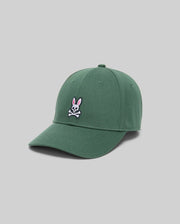 The Psycho Bunny MENS CLASSIC BASEBALL CAP (B6A816A1HT) is a green cotton cap with a white skull and crossbones and pink bunny ears, adjustable fit, curved brim, shown against a plain light gray background.