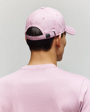 A person wearing a Psycho Bunny MENS CLASSIC BASEBALL CAP - B6A816A1HT in light pink with an embroidered Bunny and a matching pink t-shirt is shown from behind against a plain light gray background.