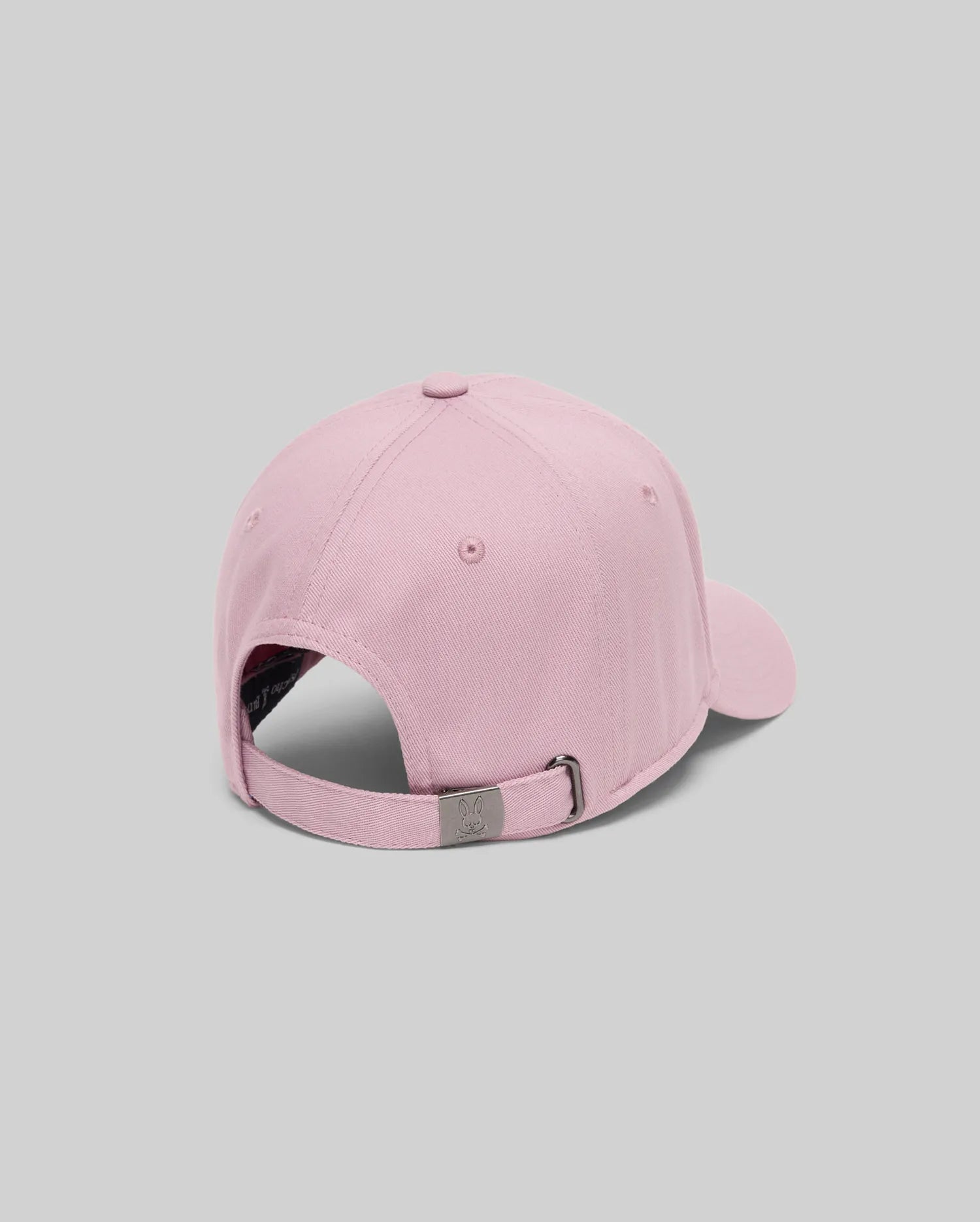 The Psycho Bunny MENS CLASSIC BASEBALL CAP - B6A816A1HT in light pink is shown from the back, highlighting its adjustable metal buckle closure, set against a plain gray background.