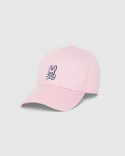 The MENS CLASSIC BASEBALL CAP - B6A816A1HT by Psycho Bunny is a timeless light pink baseball cap, meticulously crafted from 100% cotton, and showcased against a plain background. It features an embroidered design on the front, depicting a white bunny head with crossbones underneath. The bunny sports pink ears and black outlines, imparting a playful touch to this classic accessory.