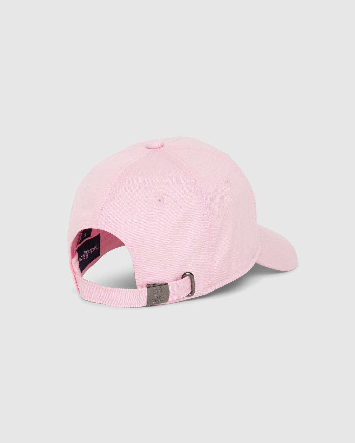 A light pink Psycho Bunny Mens Classic Baseball Cap (B6A816A1HT) is displayed from the back, showcasing an adjustable metal clasp strap. Crafted from 100% cotton, it features a dark-colored lining and a small logo on the clasp. The plain gray background accentuates the cap’s timeless design.
