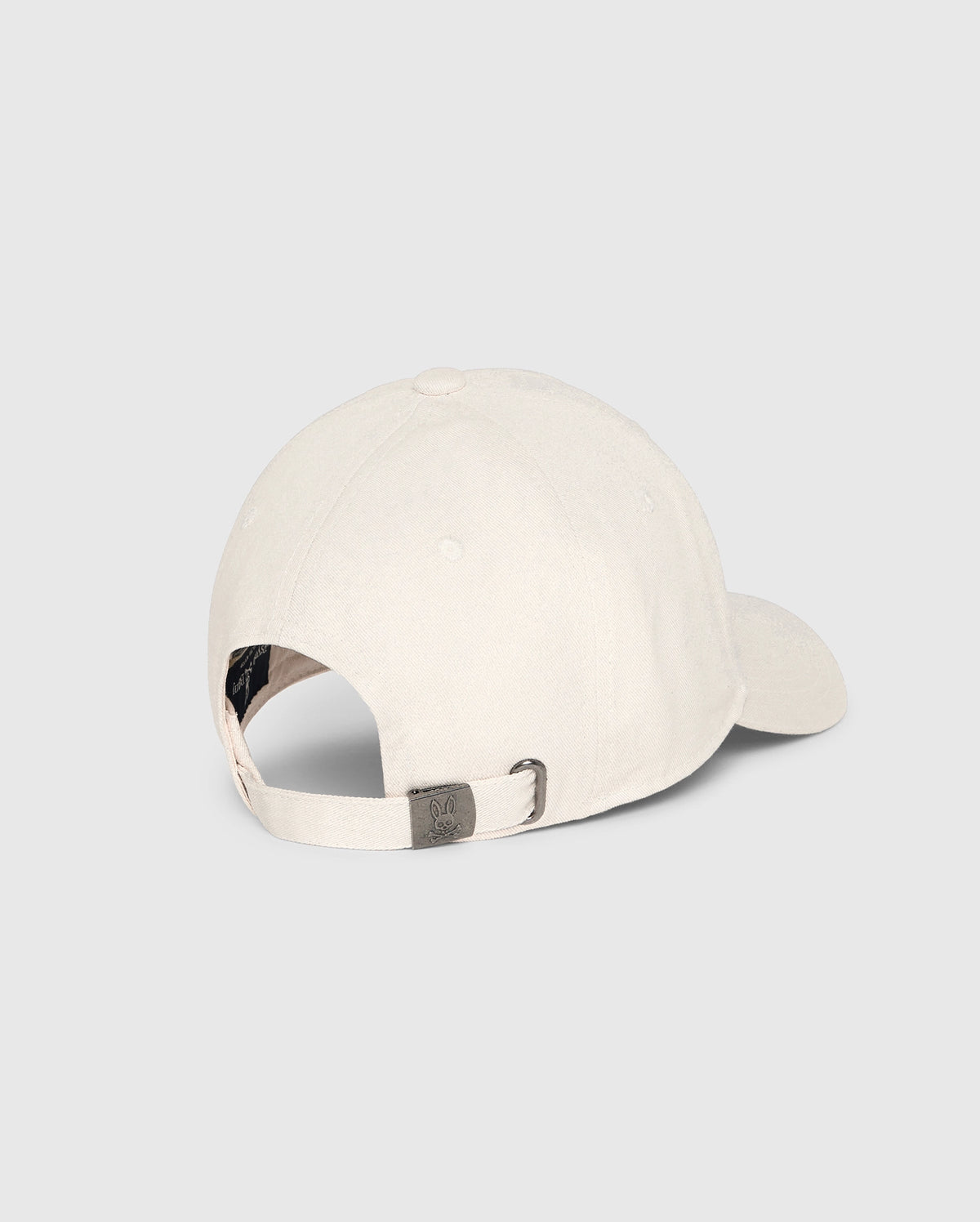 The MENS CLASSIC BASEBALL CAP - B6A816B200 by Psycho Bunny, crafted from 100% cotton in a classic beige shade, is displayed from the back against a plain light background. It boasts a curved brim, an adjustable strap with a metal clasp, and a side ventilation hole for enhanced comfort.