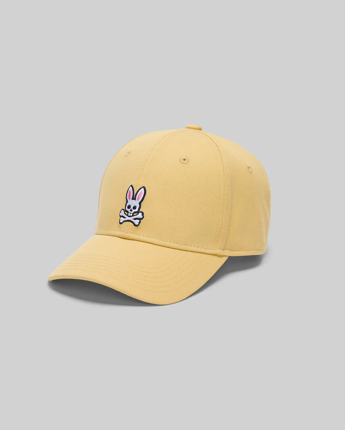 The Psycho Bunny MENS CLASSIC BASEBALL CAP - B6A816F200 is a yellow cap made from recycled polyester, featuring an adjustable fit, curved brim, and an embroidered pink rabbit face with white crossbones on the front.