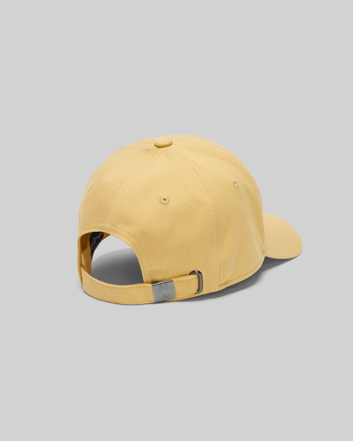 The Psycho Bunny MENS CLASSIC BASEBALL CAP (B6A816F200) in yellow is shown from the back, featuring an adjustable strap with a metal clasp, made from recycled polyester, set against a plain gray background.