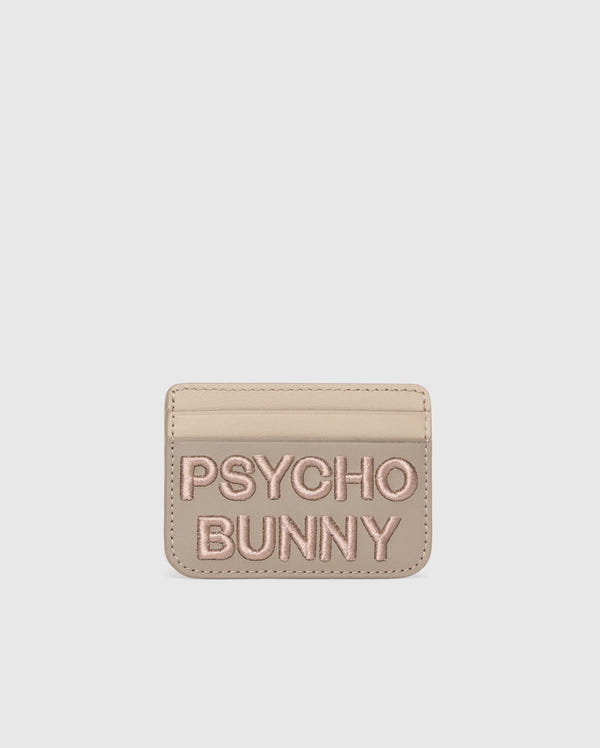 A premium beige leather cardholder features "PSYCHO BUNNY" embroidered in pink on the front. The minimalist MENS LEATHER CARD CASE - B6A869D200 by Psycho Bunny offers style and simplicity, set against a plain white background.