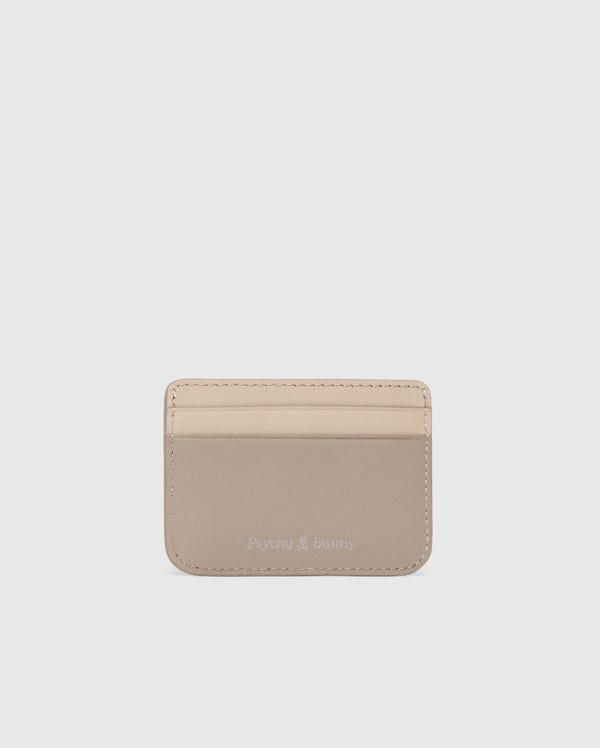 The MENS LEATHER CARD CASE - B6A869D200 by Psycho Bunny is a compact light beige leather card holder with two slots and an elegant "Psycho Bunny" embossing on the lower front. Photographed against a white background, it highlights the sleek design.