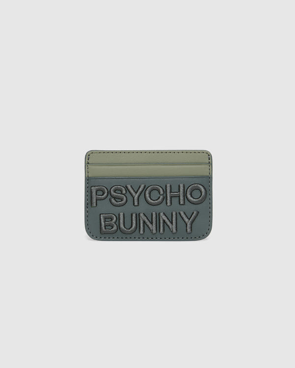 The MENS WORDMARK LEATHER CARD CASE - B6A869D200 by Psycho Bunny is a green, minimalist leather card holder made from durable shell pebble leather. It features two card slots, "PSYCHO BUNNY" embossed on the front with raised text, and a soft matte finish.