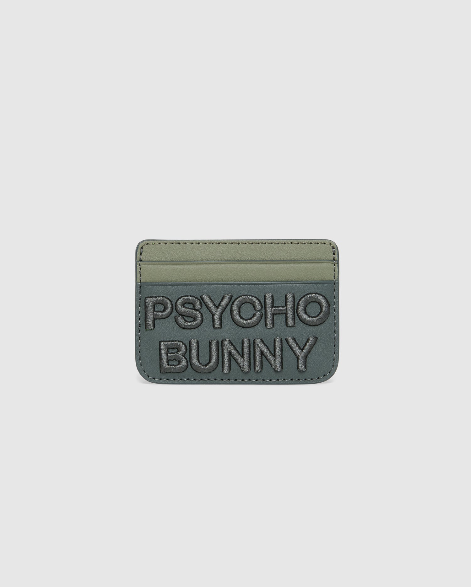 The MENS WORDMARK LEATHER CARD CASE - B6A869D200 by Psycho Bunny is a green, minimalist leather card holder made from durable shell pebble leather. It features two card slots, "PSYCHO BUNNY" embossed on the front with raised text, and a soft matte finish.