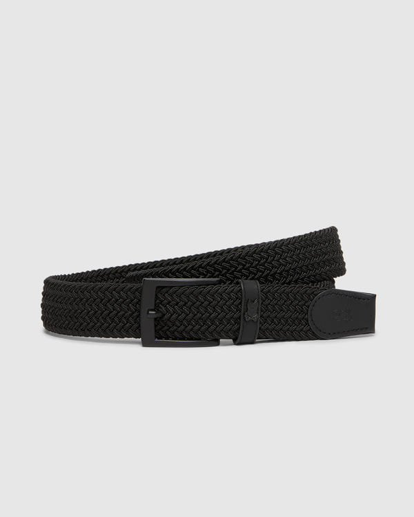 Displayed coiled on a plain light gray background, the Psycho Bunny MENS STRETCH BRAIDED BELT - B6A890F200 is a stylish black braided belt featuring a durable matte black buckle and woven texture, complemented by a small leather accent near the buckle.