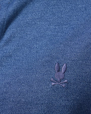 A detailed view of the MENS DALTON KNIT SHIRT by Psycho Bunny showcases a dark blue fabric with a subtle texture and an embroidered bunny head above crossed bones in lighter blue thread. Made from luxurious Peruvian Pima cotton, this shirt offers exceptional softness and comfort.