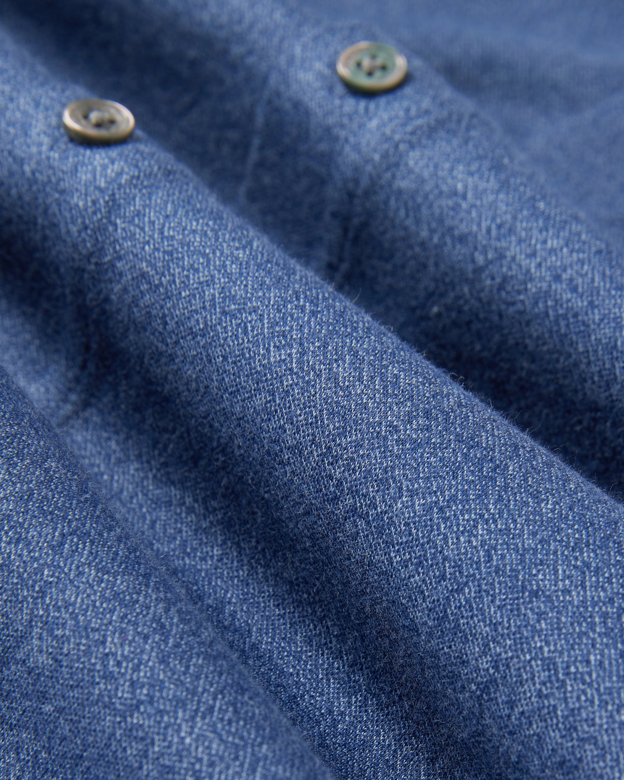 The Psycho Bunny "Mens Dalton Knit Shirt" (B6C747D200) features a textured blue denim fabric with two metallic buttons, combining ruggedness with softness akin to luxurious Peruvian Pima cotton.