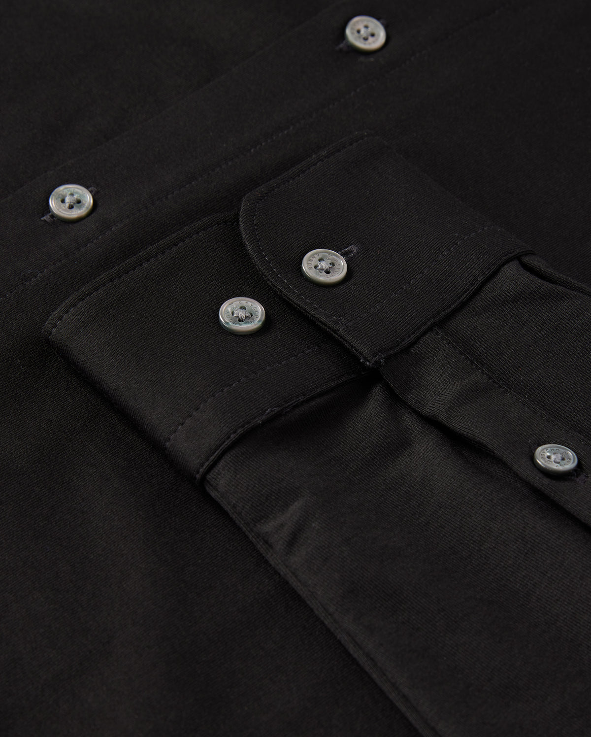 Close-up of a black MENS ARTHUR JERSEY SHIRT by Psycho Bunny, meticulously crafted from comfortable shirting and featuring a buttoned flap pocket. The shirt is neatly arranged, showcasing the fabric's texture and shiny black buttons.