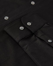 Close-up of a black MENS ARTHUR JERSEY SHIRT by Psycho Bunny, meticulously crafted from comfortable shirting and featuring a buttoned flap pocket. The shirt is neatly arranged, showcasing the fabric's texture and shiny black buttons.