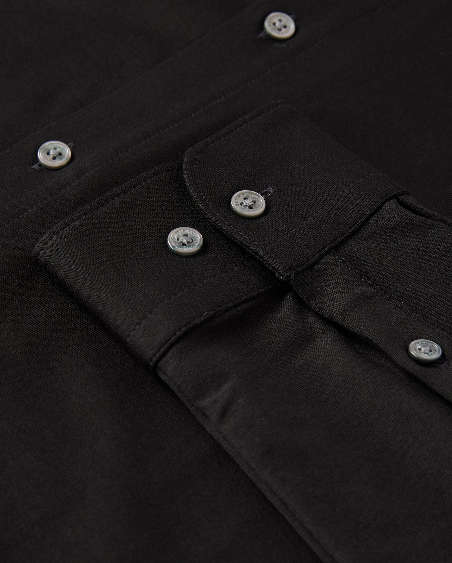 Close-up of a black MENS ARTHUR JERSEY SHIRT by Psycho Bunny, meticulously crafted from comfortable shirting and featuring a buttoned flap pocket. The shirt is neatly arranged, showcasing the fabric's texture and shiny black buttons.