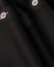Close-up of the MENS ARTHUR JERSEY SHIRT - B6C748D200 in black, designed by Psycho Bunny, crafted from comfortable shirting. It features two silver buttons with pink thread detailing. The smooth fabric is well-tailored, showcasing fine stitching and subtle folds.