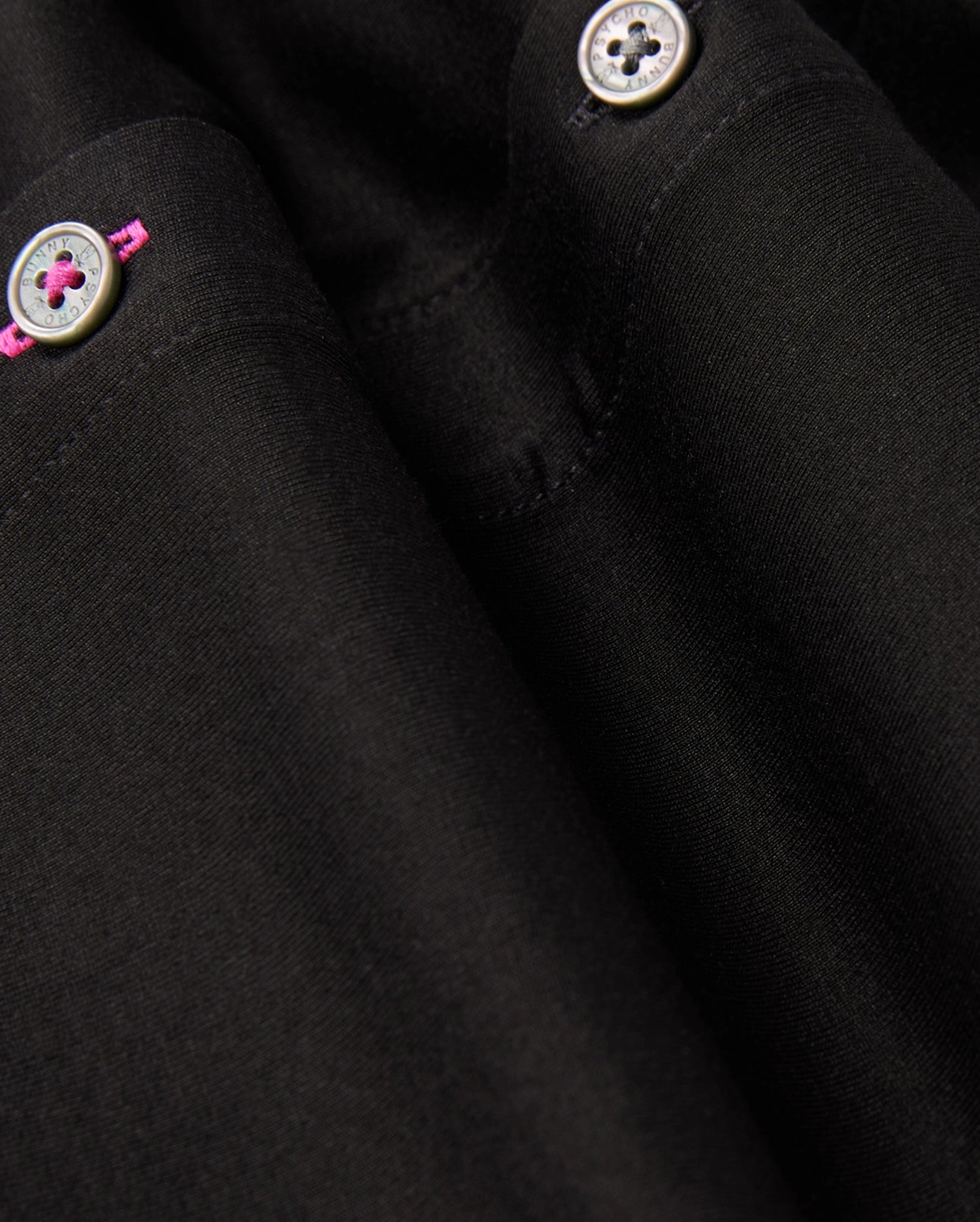 Close-up of the MENS ARTHUR JERSEY SHIRT - B6C748D200 in black, designed by Psycho Bunny, crafted from comfortable shirting. It features two silver buttons with pink thread detailing. The smooth fabric is well-tailored, showcasing fine stitching and subtle folds.