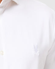 Close-up of the Psycho Bunny men's Arthur jersey shirt in stretch Pima cotton, highlighting a small embroidered bunny logo with crossed bones on the chest. This white shirt, product number B6C748D200, features a collar with partially visible button details, combining comfort and style with its jersey fabric.