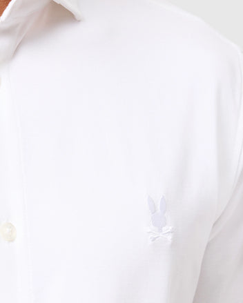 Close-up of the Psycho Bunny men's Arthur jersey shirt in stretch Pima cotton, highlighting a small embroidered bunny logo with crossed bones on the chest. This white shirt, product number B6C748D200, features a collar with partially visible button details, combining comfort and style with its jersey fabric.