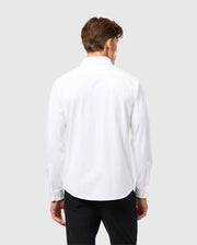 A man with brown hair is facing away, wearing a Psycho Bunny MENS ARTHUR JERSEY SHIRT - B6C748D200 crafted from stretch Pima cotton, paired with black pants against a light gray background.