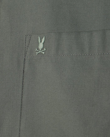 Close-up of the Psycho Bunny MENS JARED COTTON MODAL SHIRT, highlighting a pocket with an embroidered rabbit and crossbones motif in green on a muted green background.