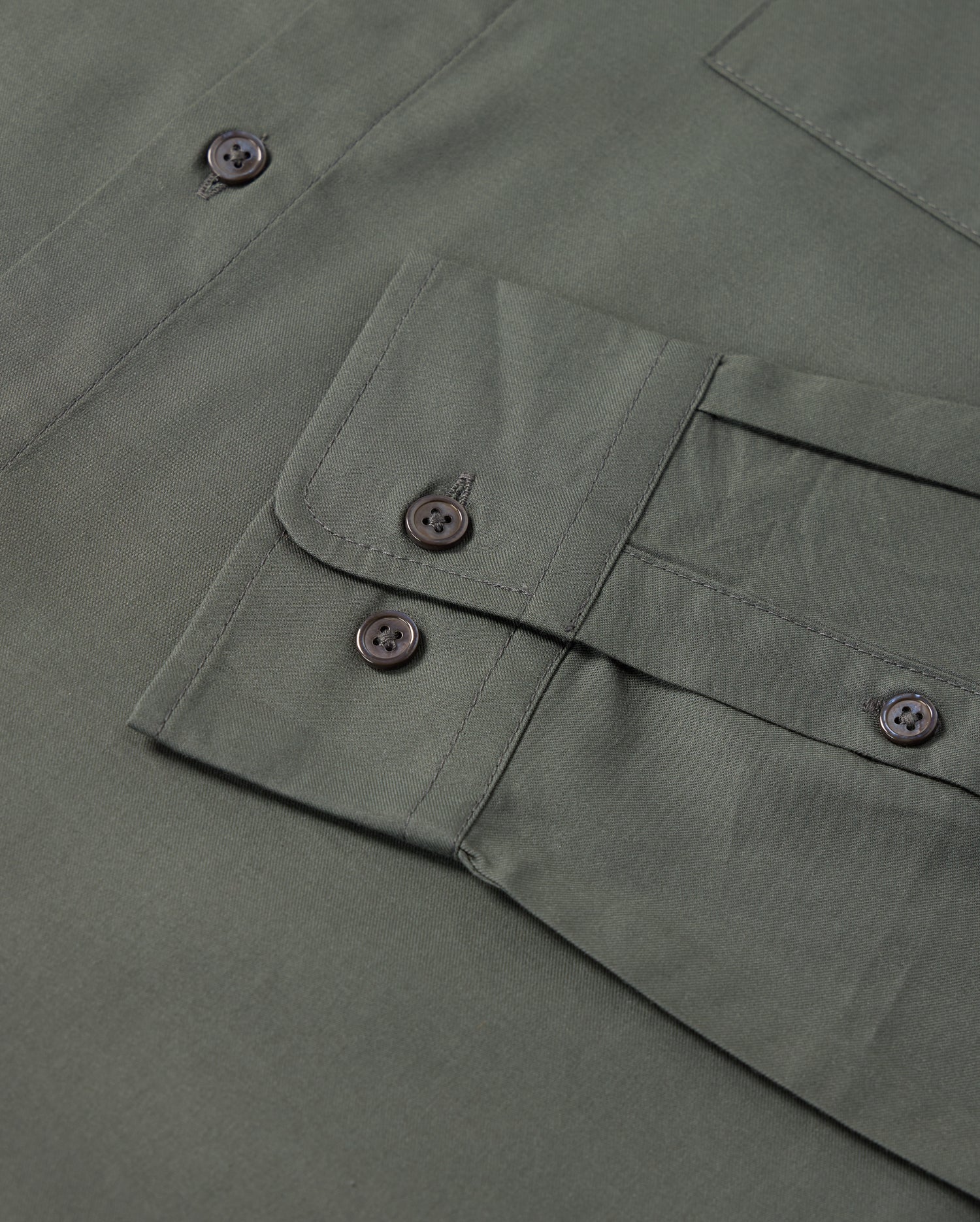 Close-up of a green fabric with a flap pocket and four black buttons from the Psycho Bunny MENS JARED COTTON MODAL SHIRT. The premium cotton modal fabric appears smooth and neatly stitched, showcasing a visible part of this men's garment.