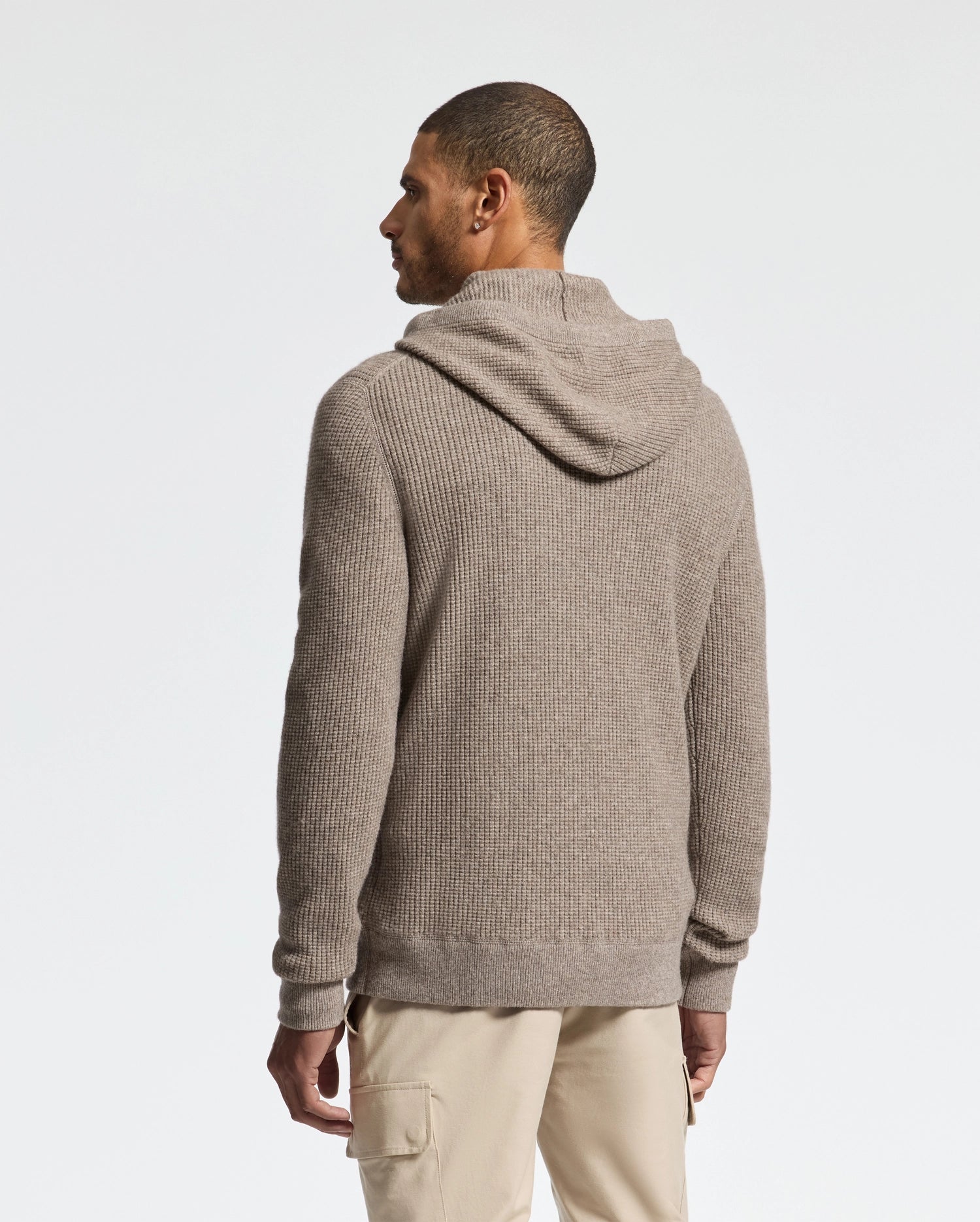 A man stands facing away, wearing the Psycho Bunny MENS LEVAN WAFFLE HOODED SWEATER and beige pants against a plain white background.