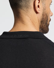 A person with short hair and a beard is shown from behind, wearing the Psycho Bunny MENS JOHNNY COLLAR SWEATER - B6E258E200 in black. The sleek look, featuring "PSYCHO BUNNY" subtly embroidered on the back of the collar, stands out against the plain white background.
