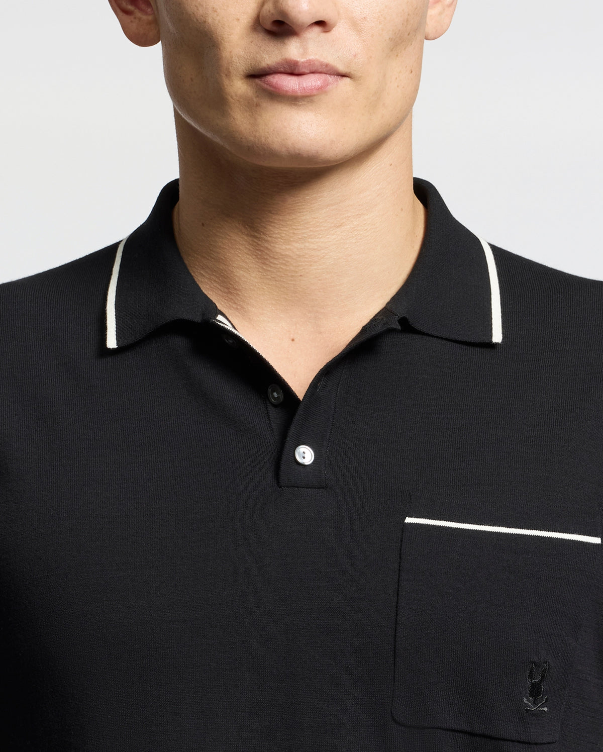 A person is wearing a Psycho Bunny Men's Longford Fine Knit Polo (B6E500F200), featuring an embroidered Bunny on the pocket, with white trim on the collar and pocket edge, all set against a plain white background.
