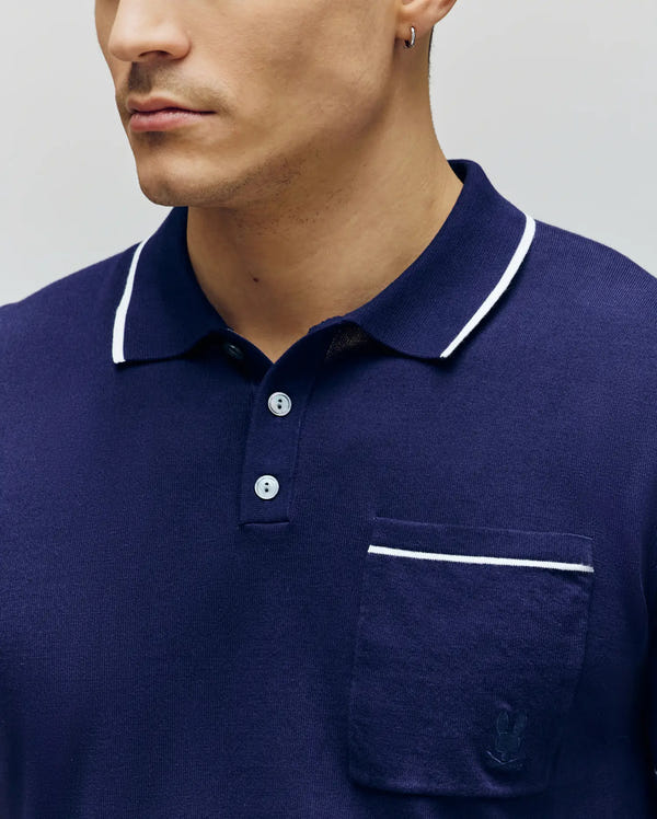 A man wears the Psycho Bunny MENS LONGFORD FINE KNIT POLO (B6E500F200) in navy with white trim and a subtle embroidered chest pocket logo. Only the lower half of his face is visible.