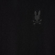 Close-up of the MENS BELMORE EXTRA FINE COTTON SWEATER by Psycho Bunny, showcasing its premium stitching and a subtly embroidered bunny logo above crossed bones on black fabric. The monochrome design seamlessly blends into the texture of extrafine cotton material.
