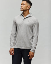 A man wears the Psycho Bunny MENS BRADSHAW POLO SWEATER (B6E835D200), a light gray merino wool polo featuring a small black and white bunny graphic on the chest, standing against a plain light background looking upward to his right.