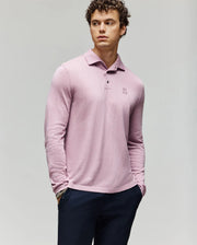 A young man with curly hair wears the Psycho Bunny MENS BRADSHAW POLO SWEATER (B6E835D200) in light pink, featuring a chest embroidered logo and mother of pearl buttons, paired with dark pants against a plain light gray background.