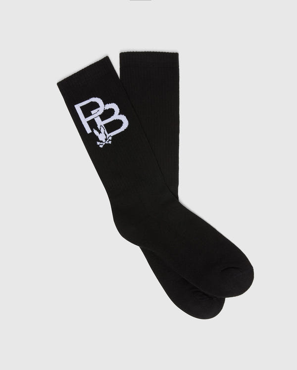 The Psycho Bunny MENS PB SPORT SOCK - B6F501F200 features a sporty flex design in black with a white PB logo and small graphic. Made from Pima cotton for superior comfort, the socks are laid flat, one overlapping the other, on a light gray background.