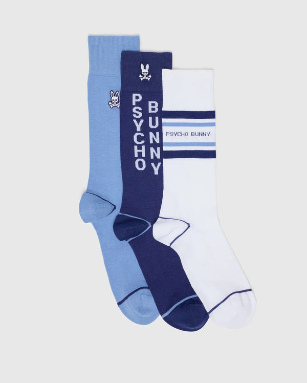 The MENS 3 PACK DRESS SOCK B6F504F200 by Psycho Bunny includes a light blue pair with a small logo, a navy pair featuring vertical "PSYCHO BUNNY" text and logo, and a white pair with navy stripes and horizontal "PSYCHO BUNNY" text—perfect for stylish ensembles.