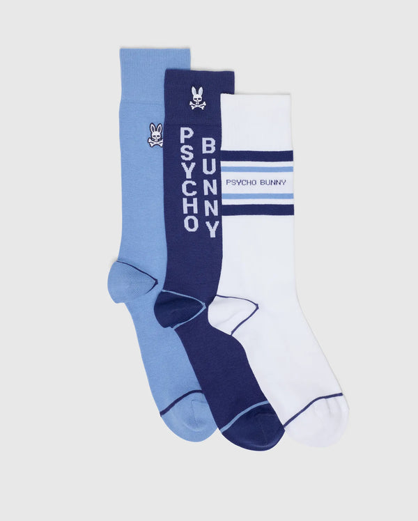 The MENS 3 PACK DRESS SOCK B6F504F200 by Psycho Bunny includes a light blue pair with a small logo, a navy pair featuring vertical "PSYCHO BUNNY" text and logo, and a white pair with navy stripes and horizontal "PSYCHO BUNNY" text—perfect for stylish ensembles.