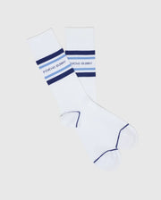 Two white dress socks with blue top stripes and the "Psycho Bunny" logo, made from Pima cotton. Featuring blue toe and heel accents, these stylish essentials are part of the MENS 3 PACK DRESS SOCK - B6F504F200 by Psycho Bunny. Perfect for enhancing any ensemble, they're displayed on a plain background.