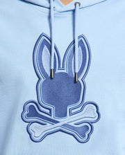 The Psycho Bunny Men's New Castle Hoodie in light blue features an embroidered bunny head with tall ears and crossed bones, resembling a playful skull and crossbones. Made from cozy French terry fabric, it includes prominent strings for added style. Model: B6H517F200.