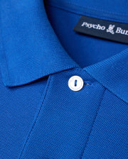 Close-up of the Psycho Bunny MENS CLASSIC PIQUE POLO SHIRT - B6K001CRPC in blue, highlighting its textured fabric. This polo features a button near the collar and an inside label with an embroidered Bunny logo. Crafted from luxurious Pima cotton, it effortlessly combines comfort with style.