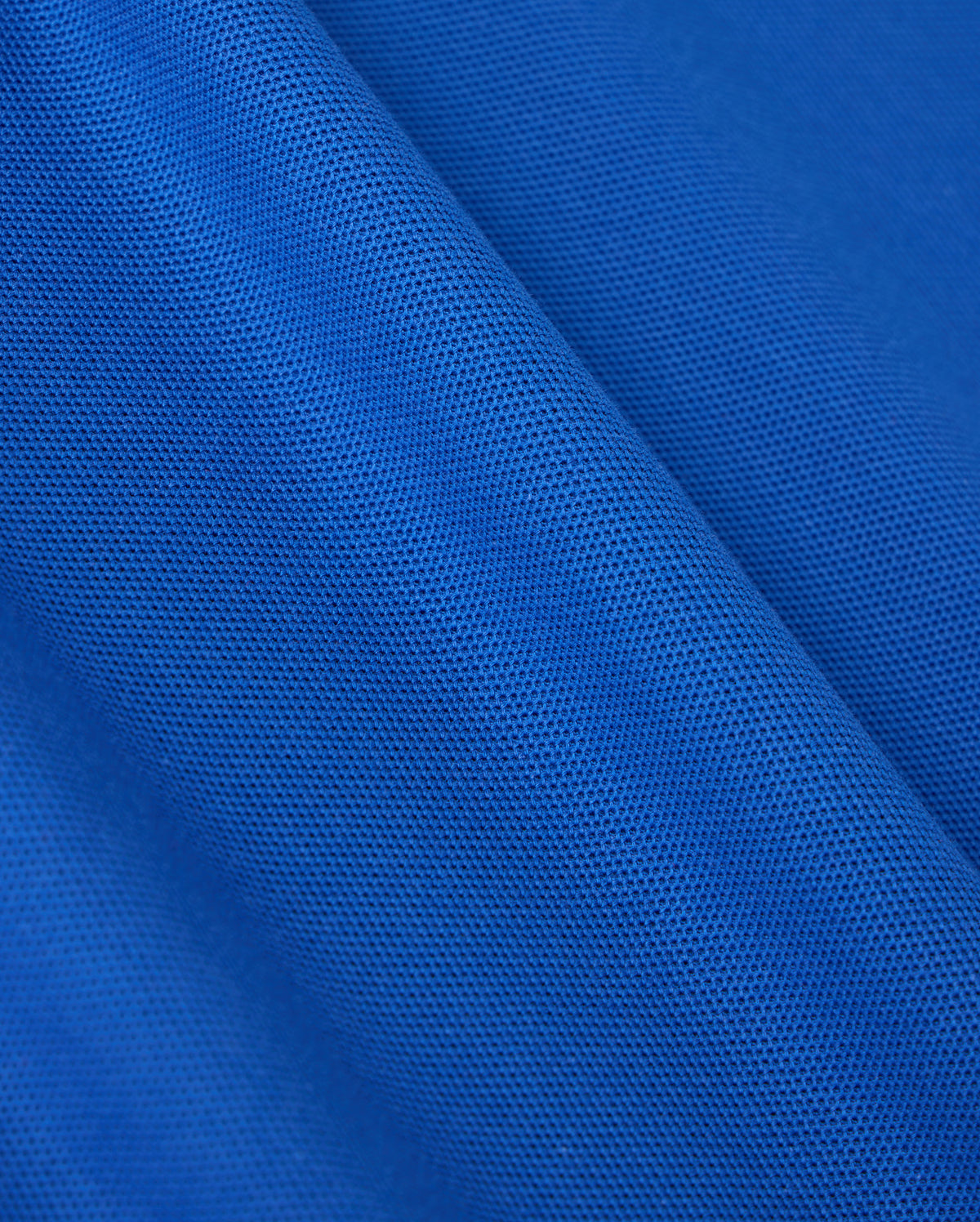 Close-up of blue fabric from the Psycho Bunny MENS CLASSIC PIQUE POLO SHIRT - B6K001CRPC, featuring a classic piqué polo texture. The material is lightweight and semi-transparent with uniformly distributed tiny holes throughout, creating a patterned appearance akin to fine Pima cotton.