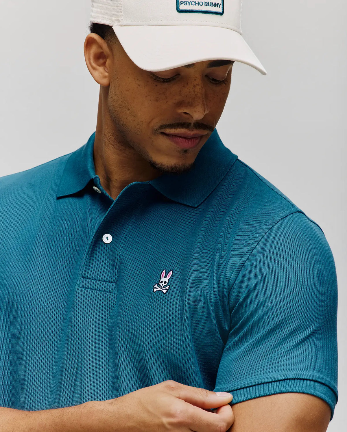 Mens Classic Pique Polo in teal, featuring a classic fit, pique knit fabric, two-button placket, and a small embroidered pink and white Psycho Bunny skull logo on the left chest.