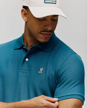 Mens Classic Pique Polo in teal, featuring a classic fit, pique knit fabric, two-button placket, and a small embroidered pink and white Psycho Bunny skull logo on the left chest.
