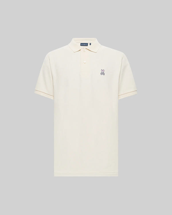The Psycho Bunny MENS CLASSIC PIQUE POLO SHIRT (B6K001F200) is a cream-colored Pima cotton polo with a collar, button placket, and embroidered Bunny logo on the left chest, shown against a plain gray background.