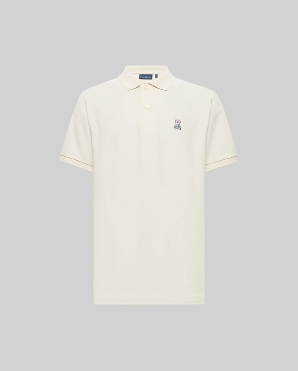 The Psycho Bunny MENS CLASSIC PIQUE POLO SHIRT (B6K001F200) is a cream-colored Pima cotton polo with a collar, button placket, and embroidered Bunny logo on the left chest, shown against a plain gray background.