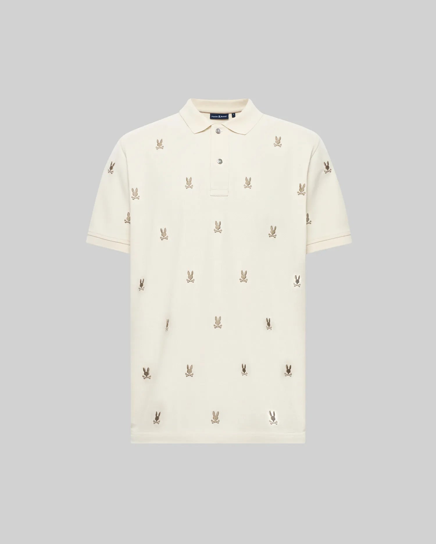 The MENS HOLLAND ALL OVER BUNNY PIQUE POLO (B6K618F200) by Psycho Bunny is a cream short-sleeve polo with a subtle collar and rows of small embroidered bunny logos, shown on a plain grey background.