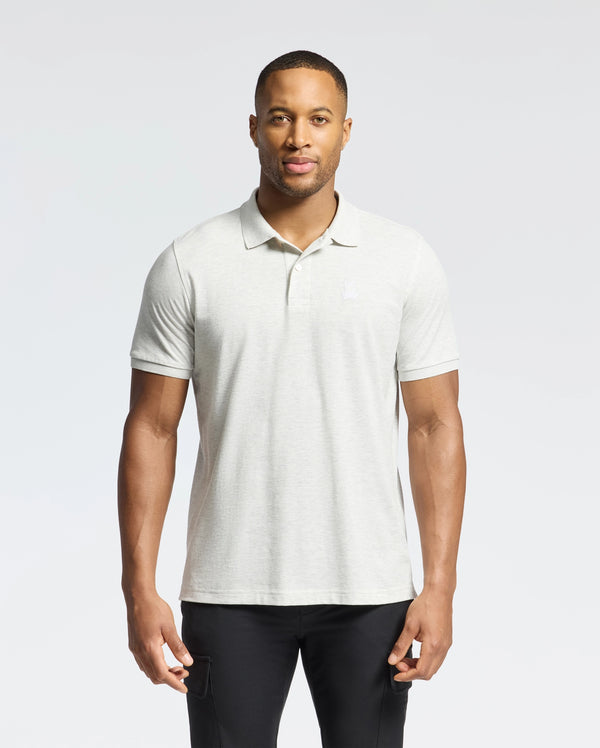 A man confidently stands against a light grey backdrop, wearing a Psycho Bunny MENS JAMES PIQUE POLO (B6K945D200) made of durable Pima cotton and black pants, facing the camera directly.